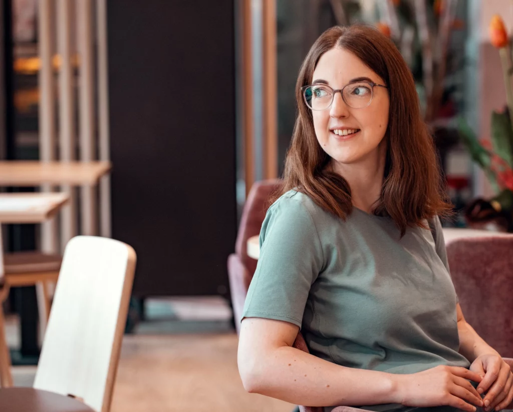 Irene Theiß sitzt lächelnd in einem Cafe und blickt nach links.